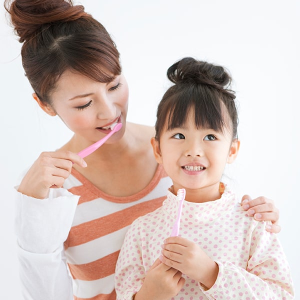A mom showing her daughter how to brush her teeth