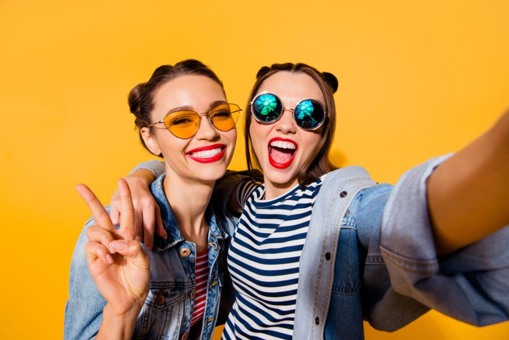 Two young females wearing sunglasses smile for a selfie after teeth whitening